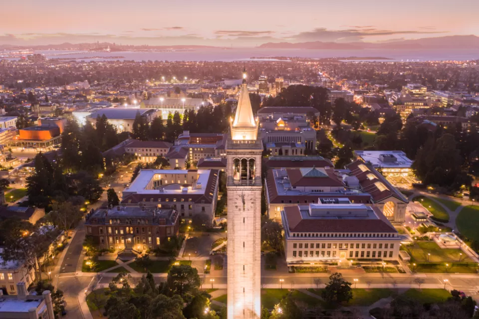 Aerial view at dusk of UC Berkeley campus with tall tower in foreground and San Francisco Bay in the background